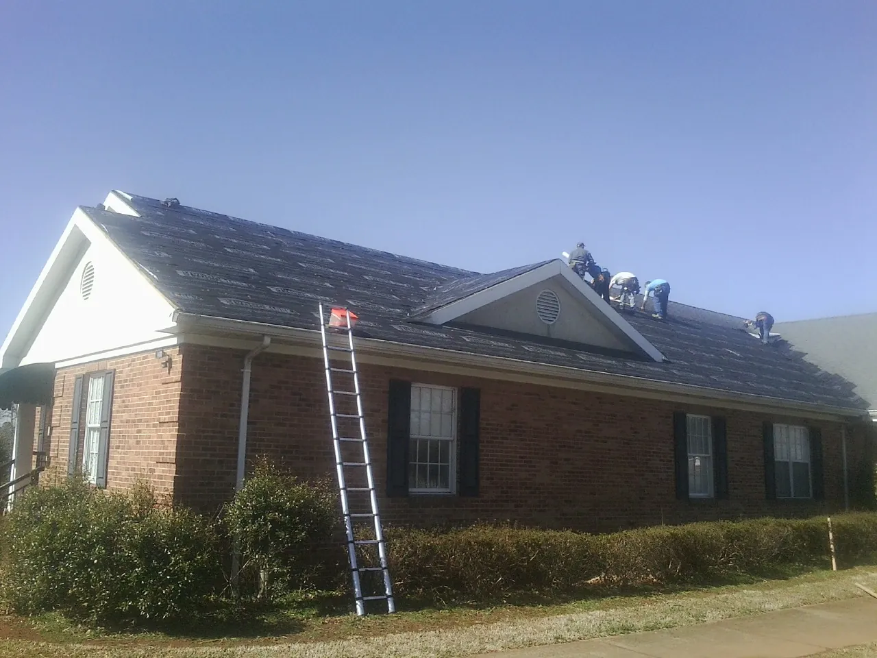 Crew tearing shingles off a brick ranch roof with a ladder set — Emergency Roof Repair work by our crew in Reisterstown