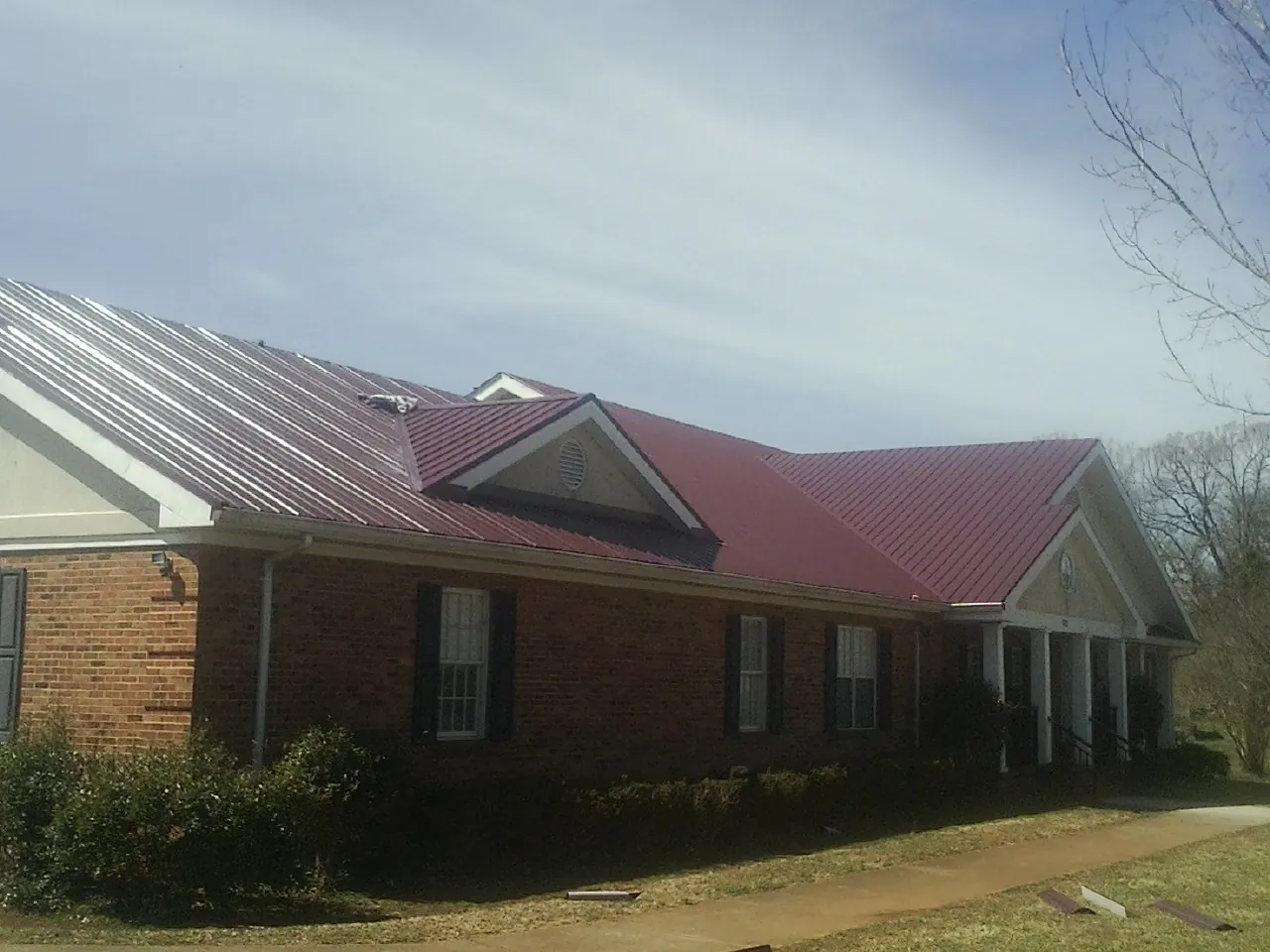 Red metal roof with gabled entries on a long brick building, from a Hail Damage Roof Repair job in Reisterstown