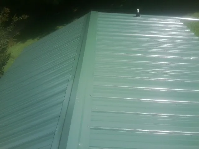 New green metal panels meeting at the ridge of a roof — Flat Roof Repair work by our crew in Reisterstown