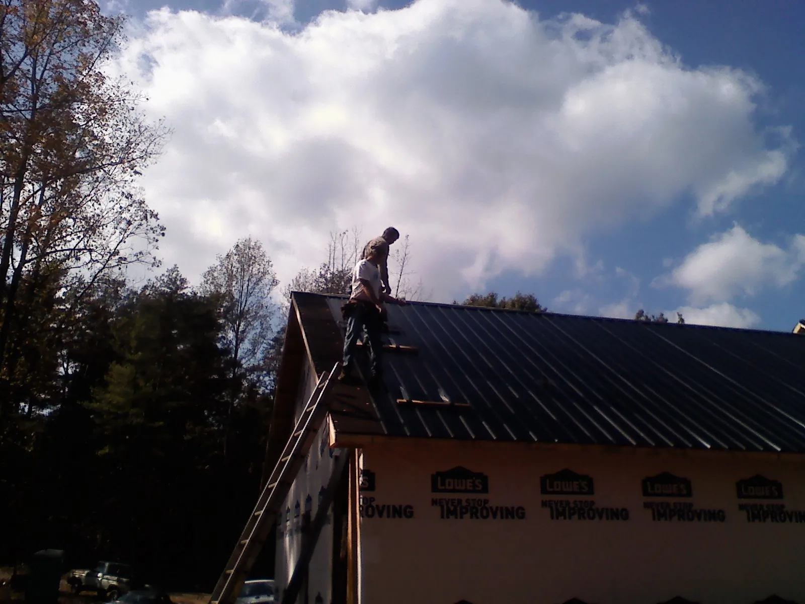 Roofer fastening dark metal panels high against a cloudy sky, from a Roof Inspection job in Reisterstown