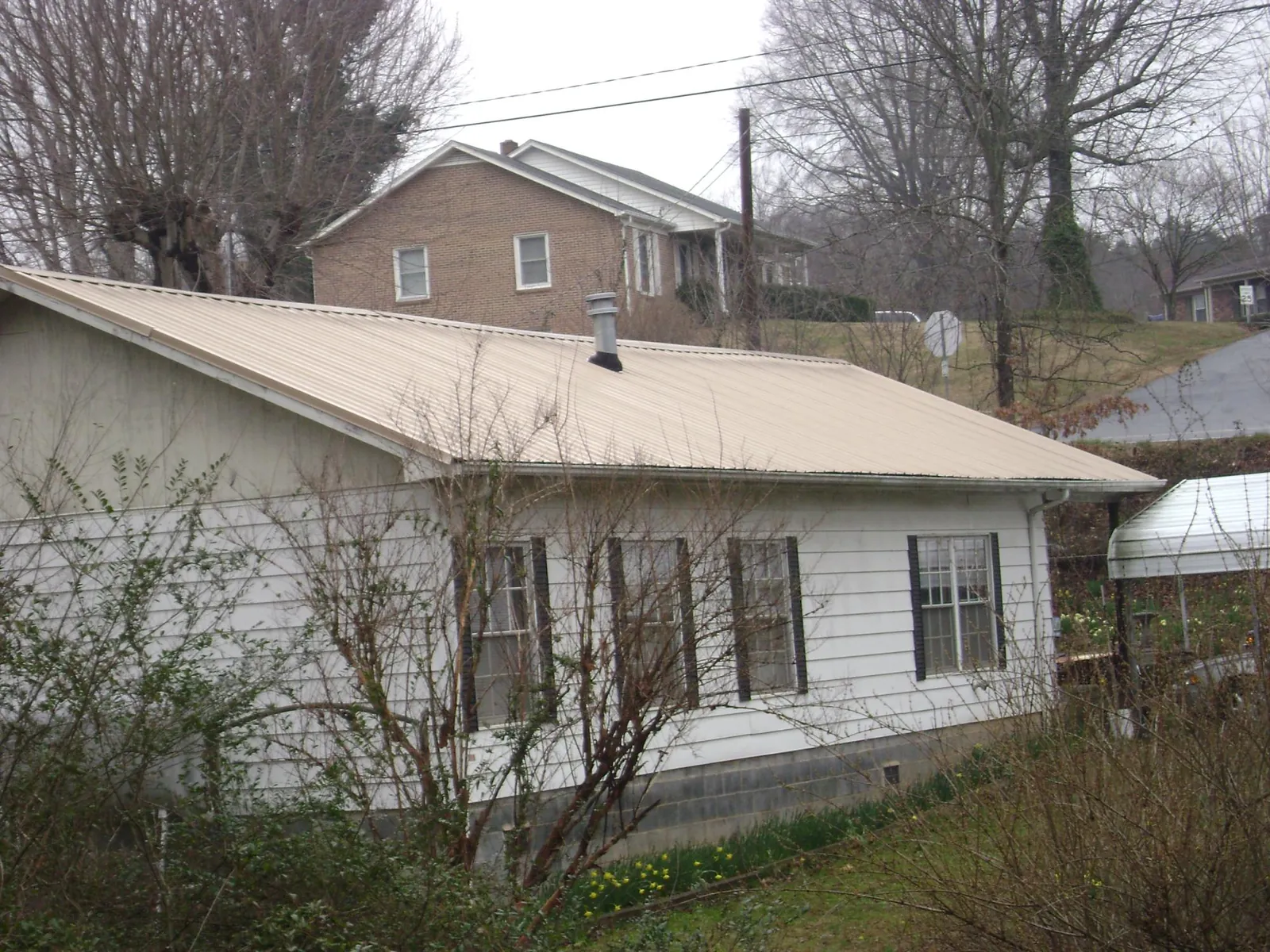 Tan metal roof on a white sided house set into a hillside — Commercial Roofing by Roofing Brothers in Reisterstown